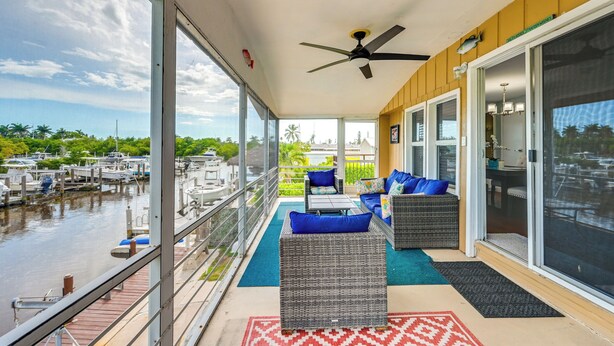 A covered outdoor area with wicker furniture, a ceiling fan, and a view of boats on the water. - 'the Waterfront Cottage' w/ Dock in Goodland! (Goodland)