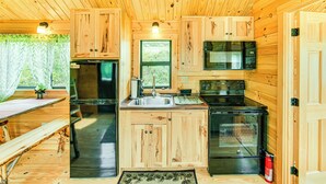 A wooden cabin interior with a kitchen area featuring a sink, stove, and microwave.