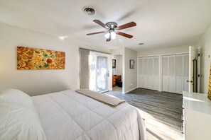 Ein Schlafzimmer mit einem Bett, einem Deckenventilator, einem Gemälde und Blick auf einen Flur mit Einbauschränken.