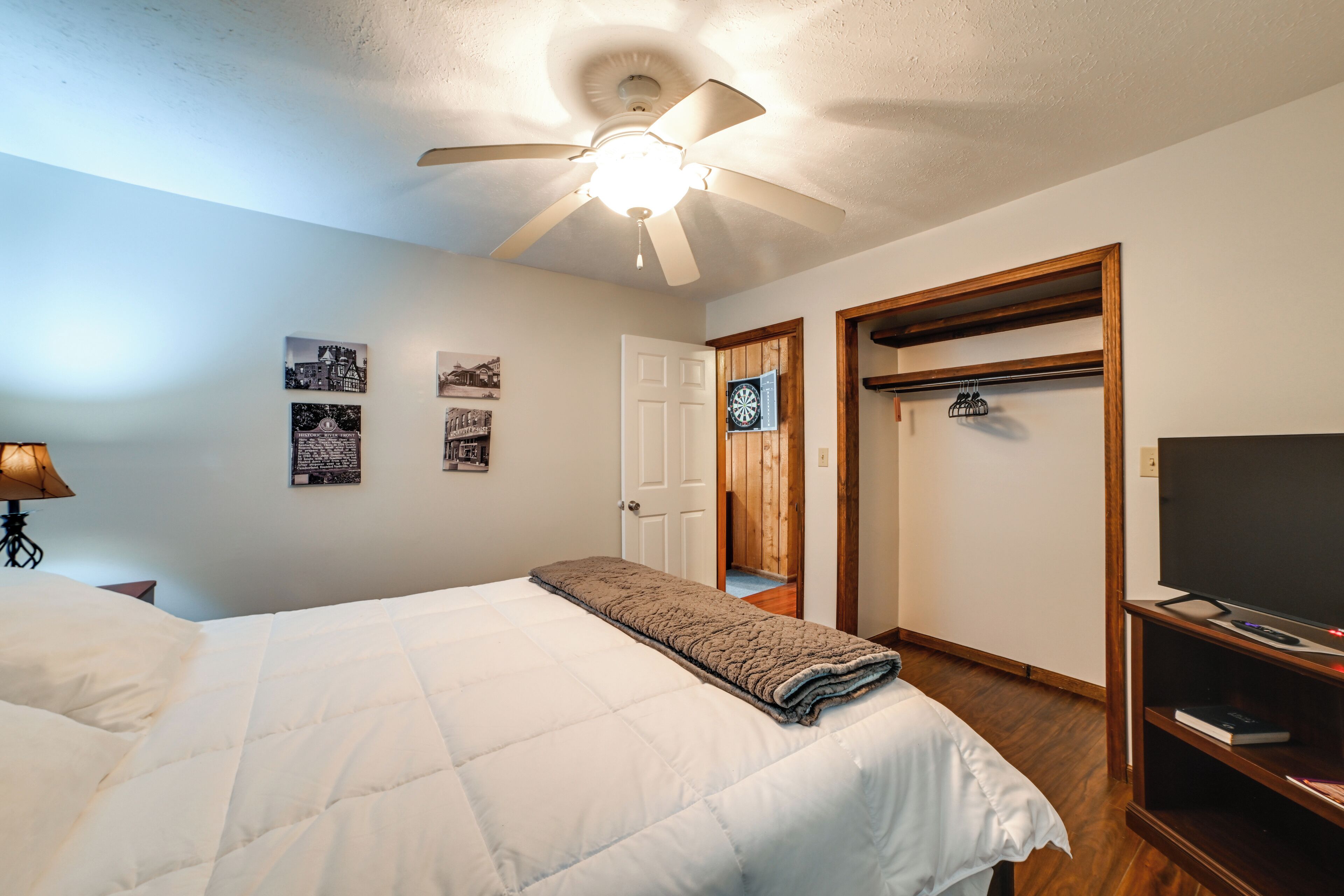A bedroom with a bed, ceiling fan, wooden wardrobe, and a television.