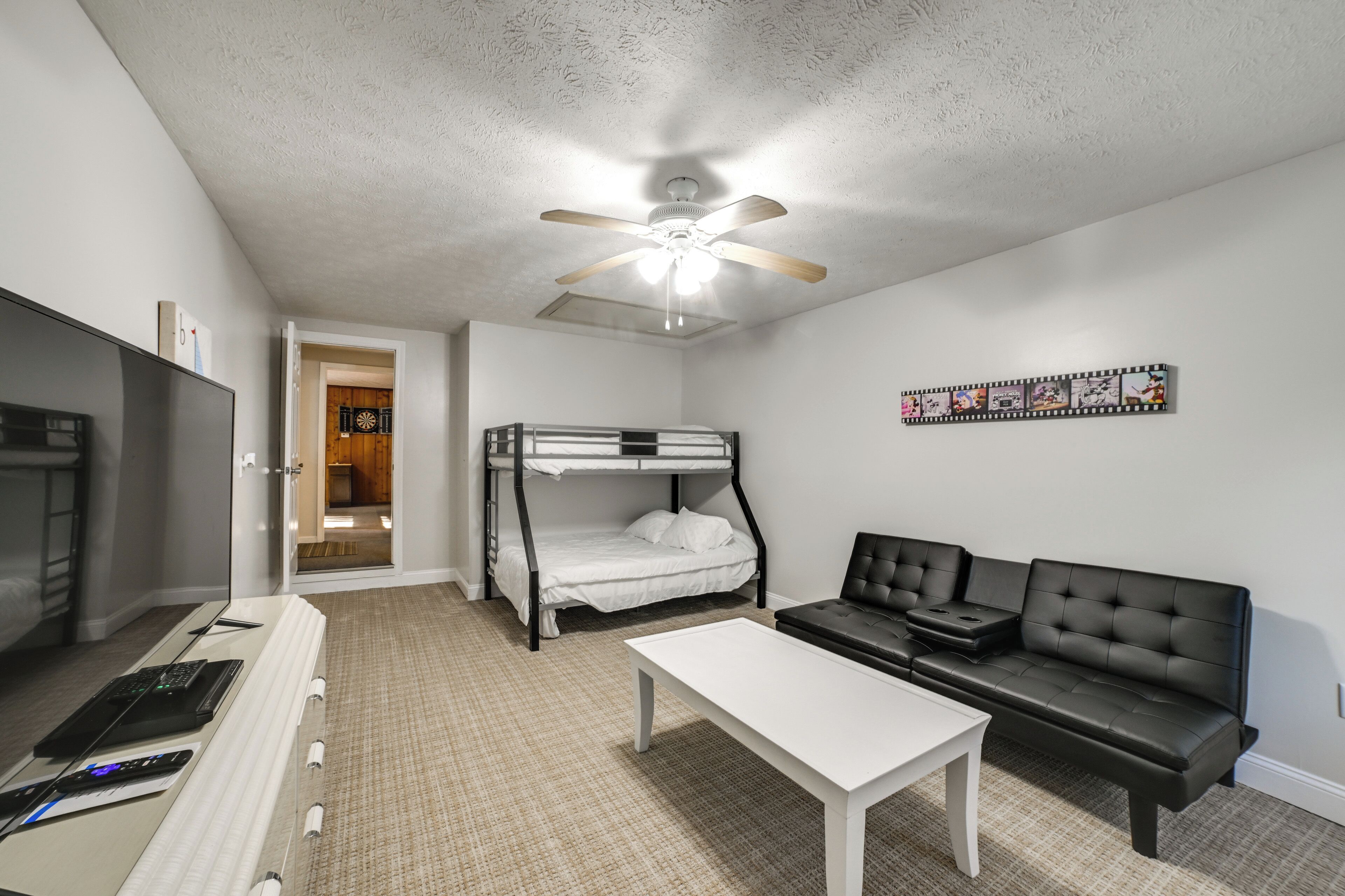 A room with a bunk bed, a sofa, a desk, and a ceiling fan.