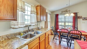 A kitchen with granite countertops, wooden cabinets, a double sink, and a dining area with a red tablecloth and black chairs. - 3 Mi to Arkansas River: Rural Family Home w/ Yard (Spiro)