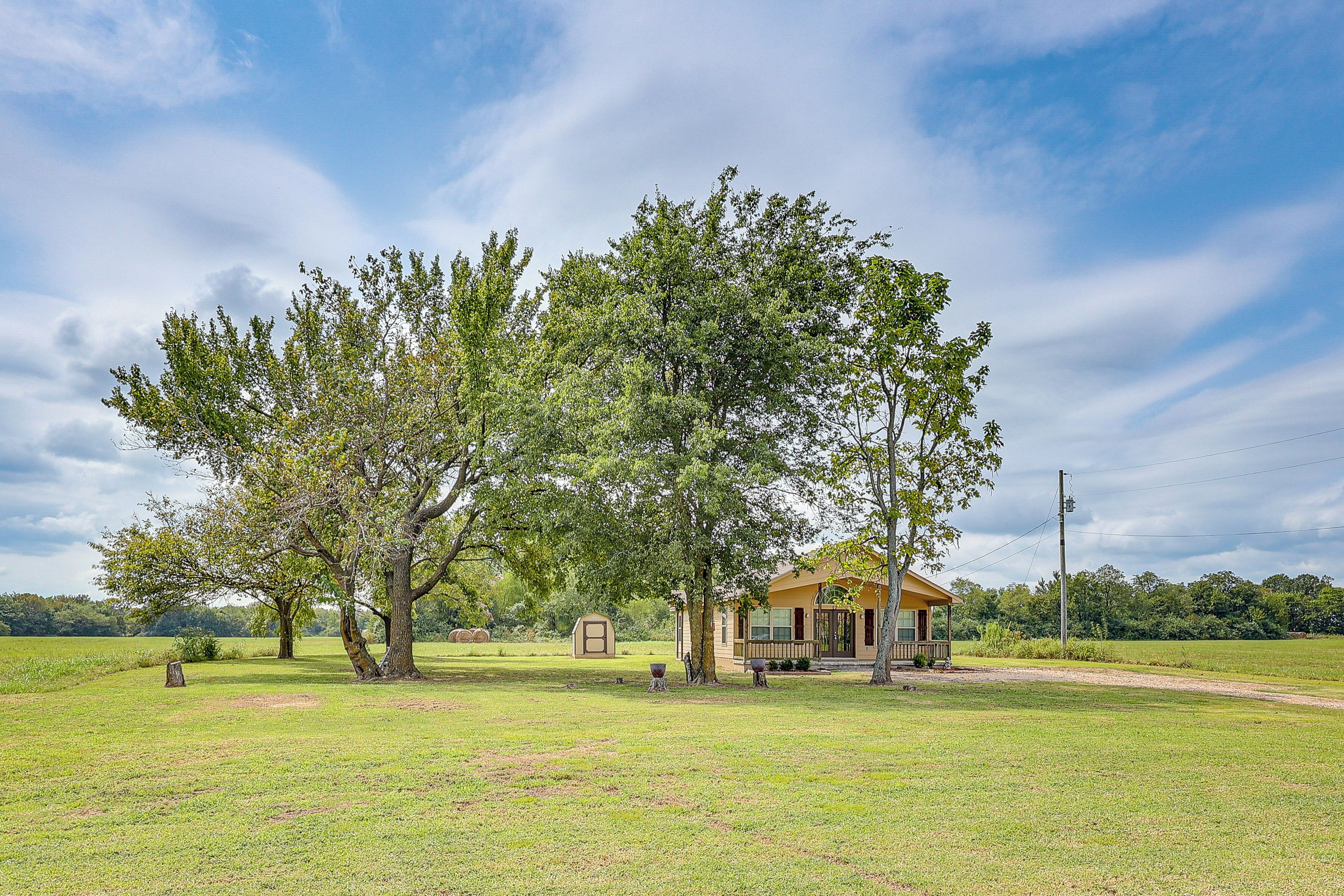 A small house with a porch, surrounded by a grassy field and trees.