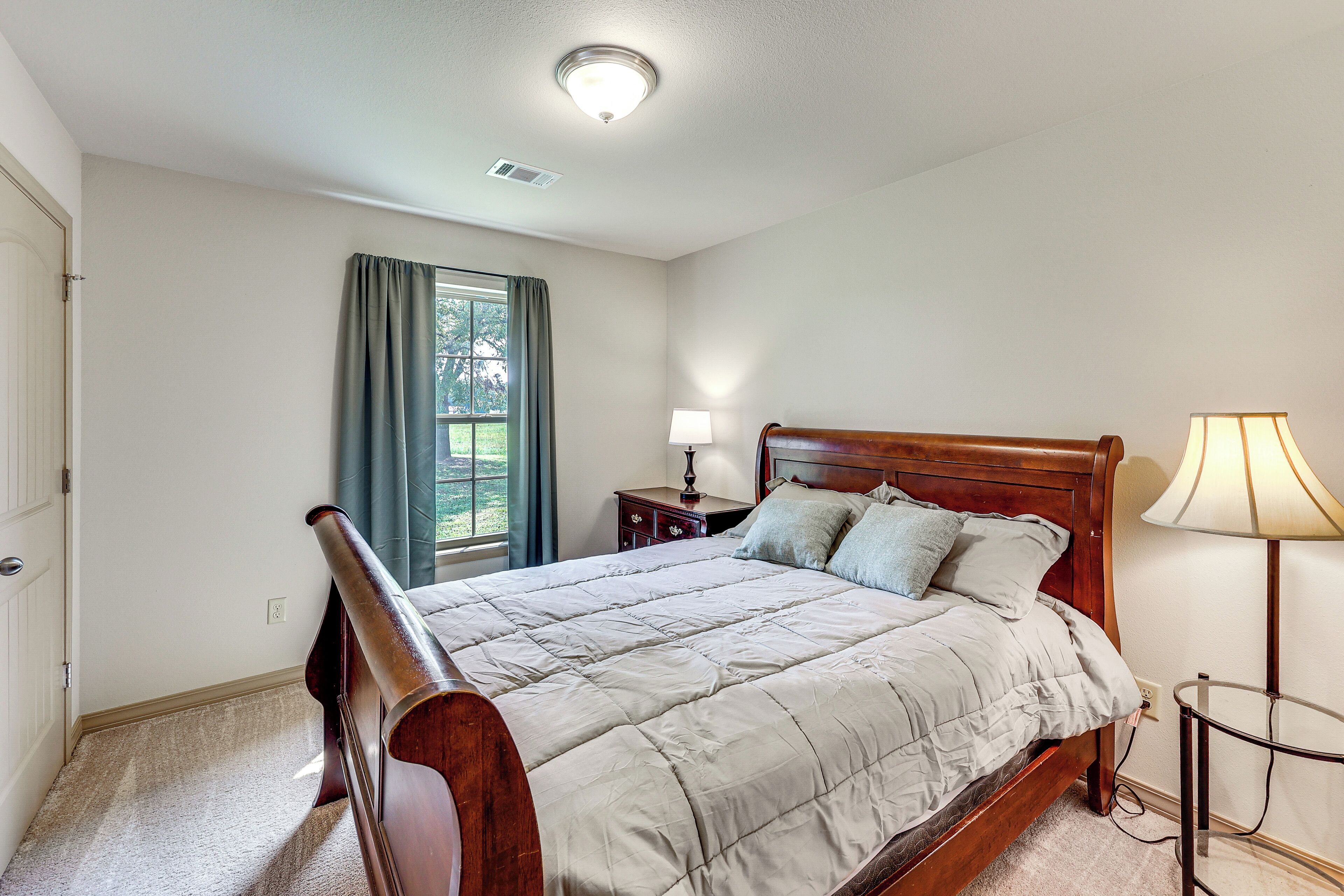A bedroom with a wooden bed, a nightstand, a lamp, and a window with curtains.