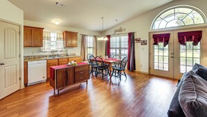 A spacious kitchen with wooden cabinets, a dining area with a red table and chairs, and a large window with curtains. - 3 Mi to Arkansas River: Rural Family Home w/ Yard (Spiro)