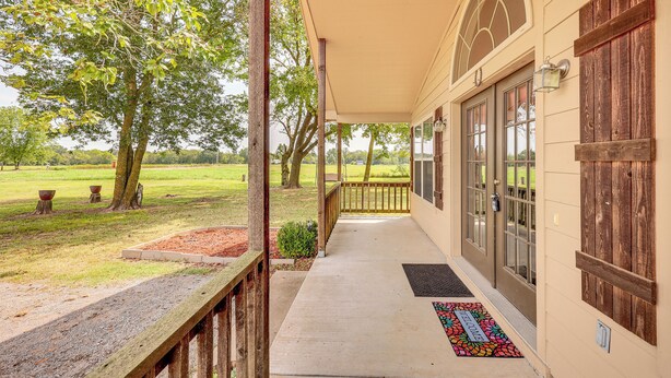A covered porch with a concrete floor, wooden railing, and a welcome mat. - 3 Mi to Arkansas River: Rural Family Home w/ Yard (Spiro)