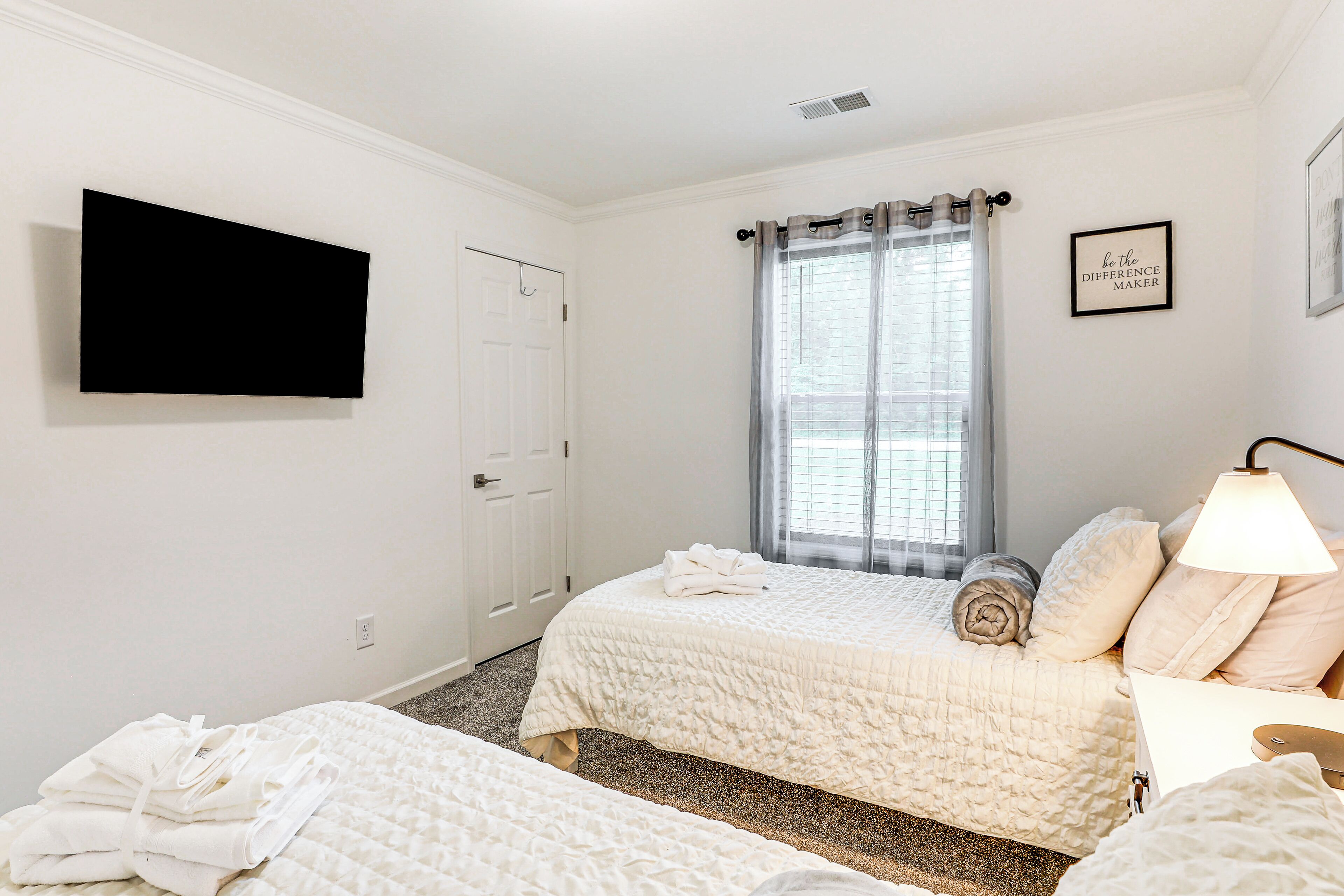 A hotel room with two beds, a television mounted on the wall, a window with curtains, and a bedside lamp.