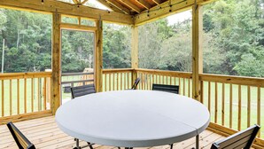 A covered outdoor deck with a round table and chairs, surrounded by wooden railings and a view of a forested area. - Screened Porch: Family-friendly St Stephen Retreat (St. Stephen)