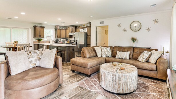 A spacious living room with a brown leather sectional sofa, a round coffee table, and a dining area with a wooden table and chairs. - Screened Porch: Family-friendly St Stephen Retreat (St. Stephen)