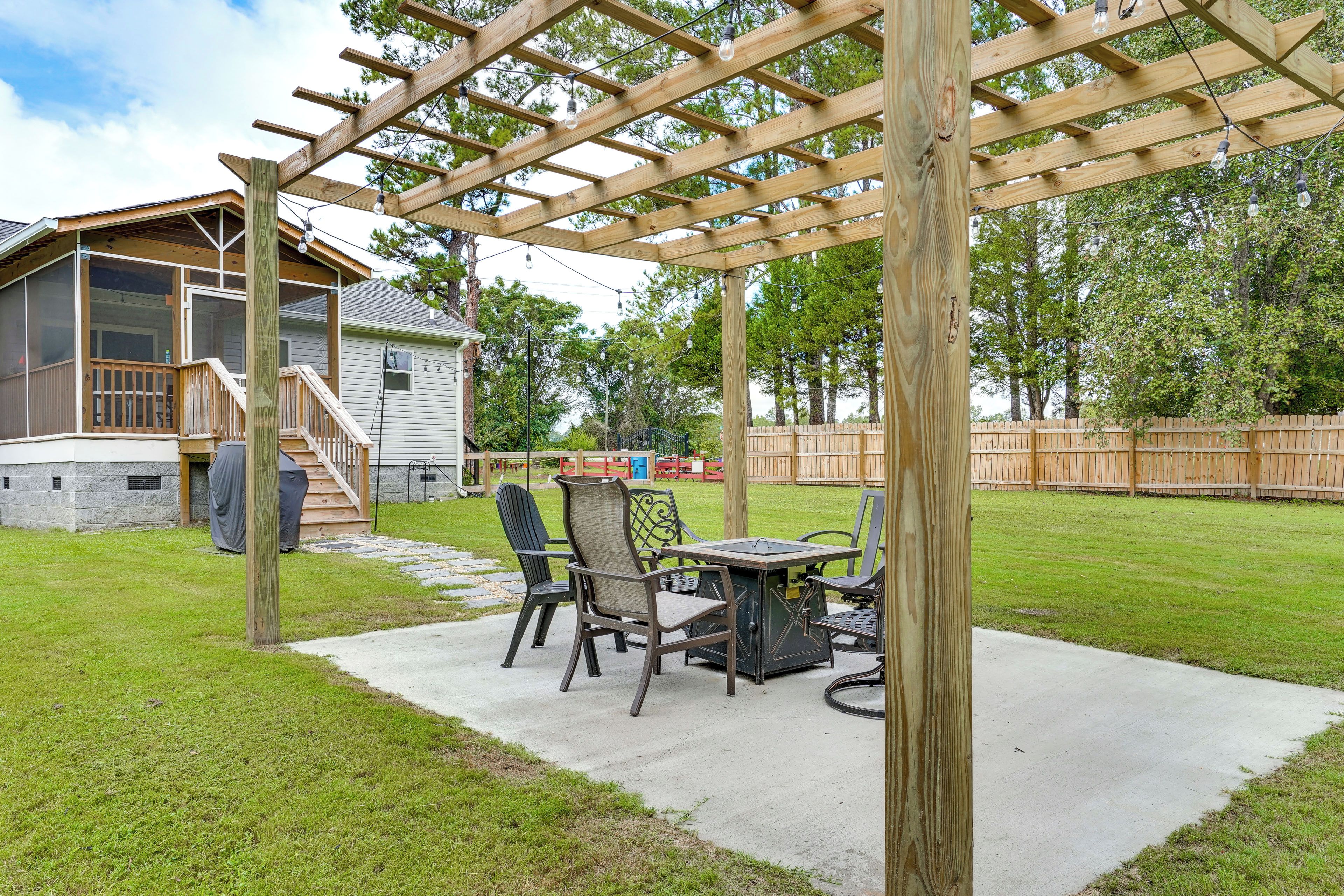 A covered patio area with a table and chairs, a pergola overhead, and a view of a house in the background.