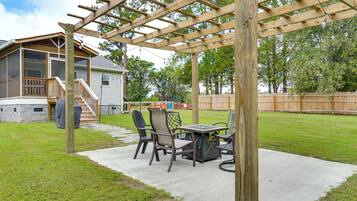 A covered patio area with a table and chairs, a pergola overhead, and a view of a house in the background.