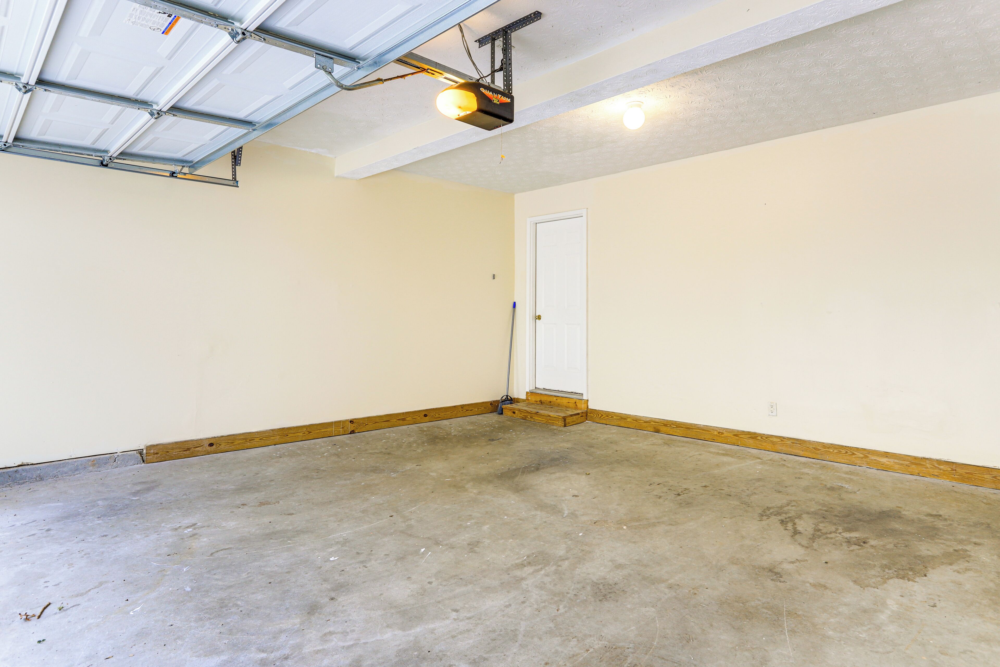 Een schone, lege garage met een betonnen vloer, een witte deur en een aan het plafond bevestigde projector.