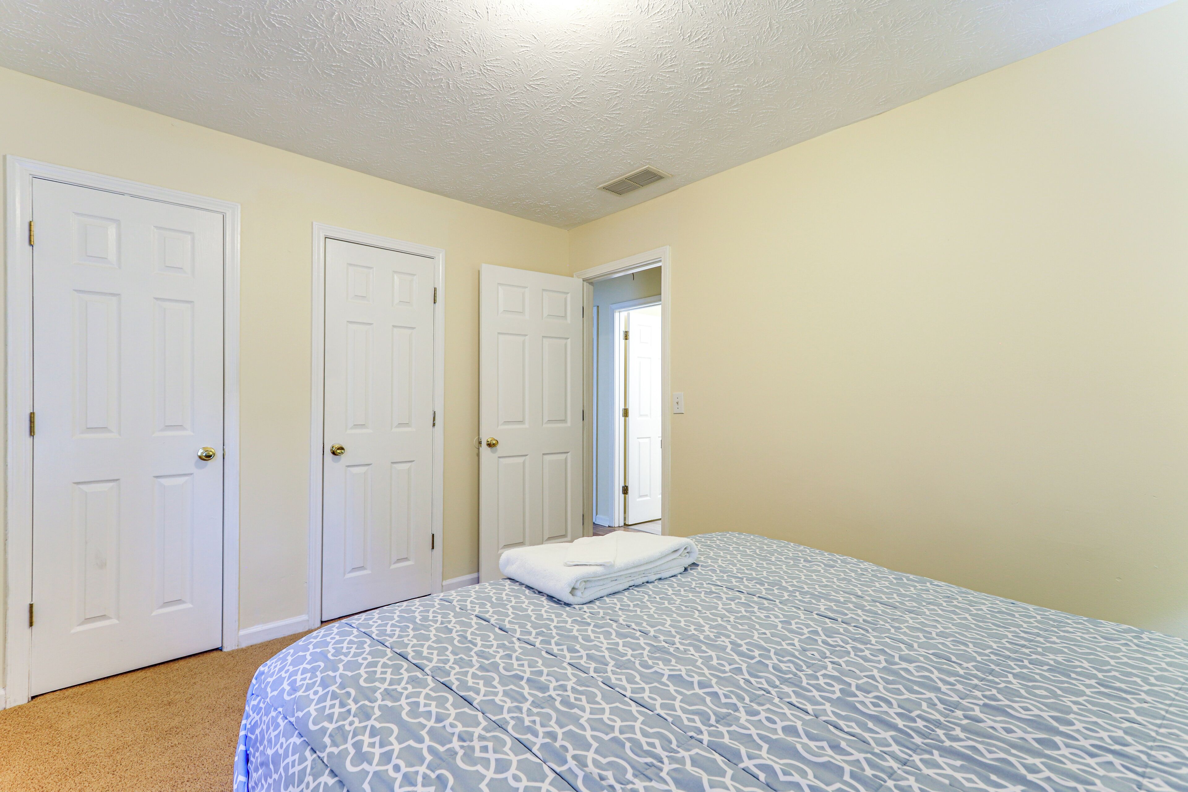 Un dormitorio con una cama, dos puertas blancas y una pared de color claro.