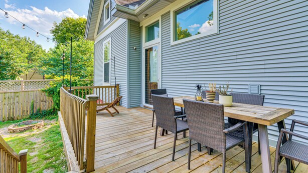 Une terrasse avec une table et des chaises en bois, un petit jardin et une maison aux murs recouverts d’un revêtement clair, avec une fenêtre.