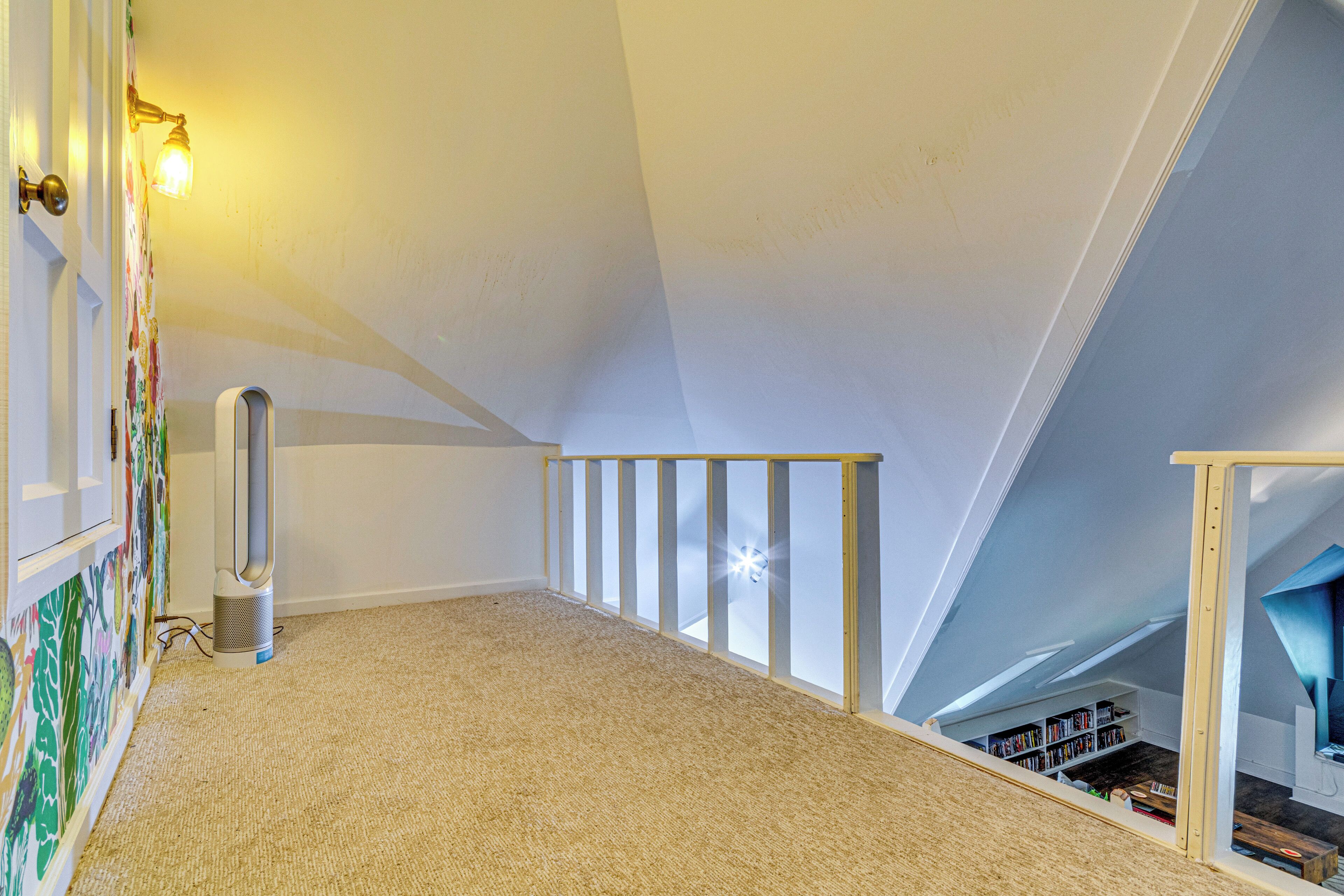 A high-ceilinged attic room with a wooden staircase, a radiator, and a bookshelf.