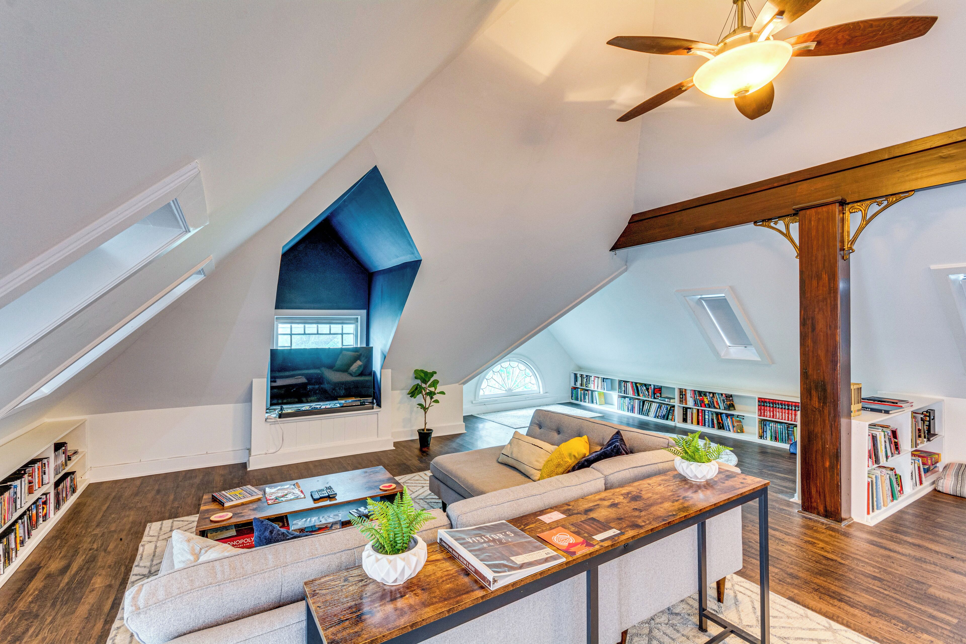 A spacious loft with a sloped ceiling, a built-in seating area, and a large collection of bookshelves.