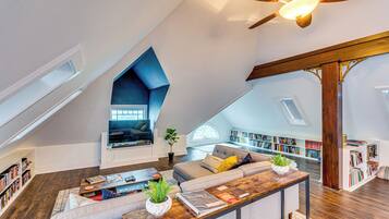 A spacious loft with a sloped ceiling, a built-in seating area, and a large collection of bookshelves.