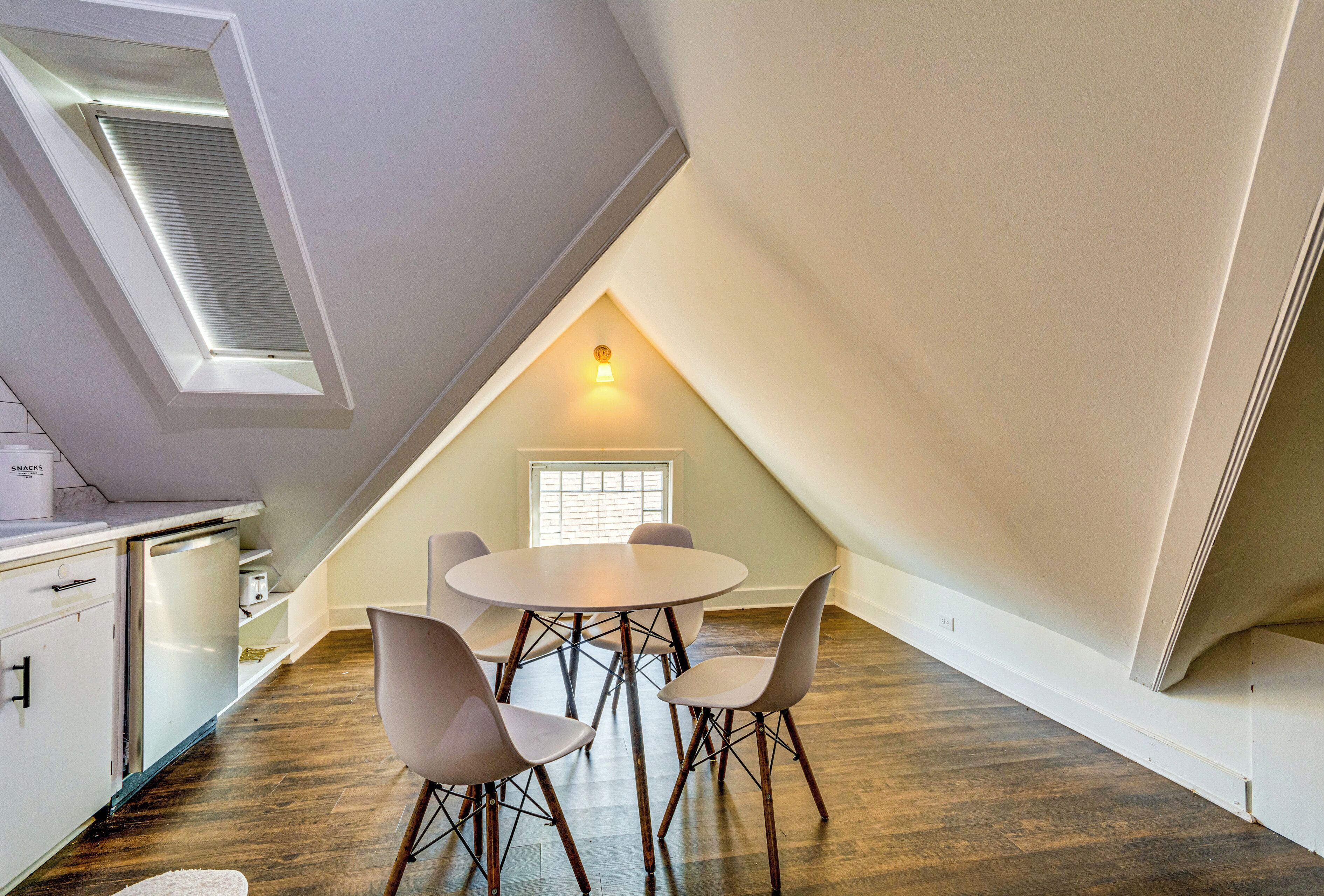 A dining area with a round table and four chairs, a small window, and a ceiling vent.