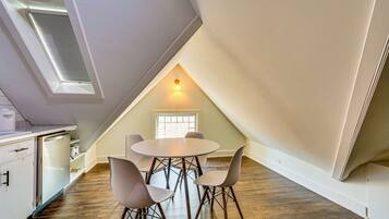 A dining area with a round table and four chairs, a small window, and a ceiling vent.