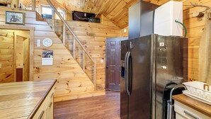 Ein Holzblockhaus-Interieur mit Küche, Kühlschrank, einer Uhr und einer Treppe.