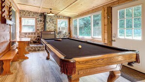 Ein Billardtisch in einem Raum mit Steinwänden, Holzbänken und großen Fenstern.