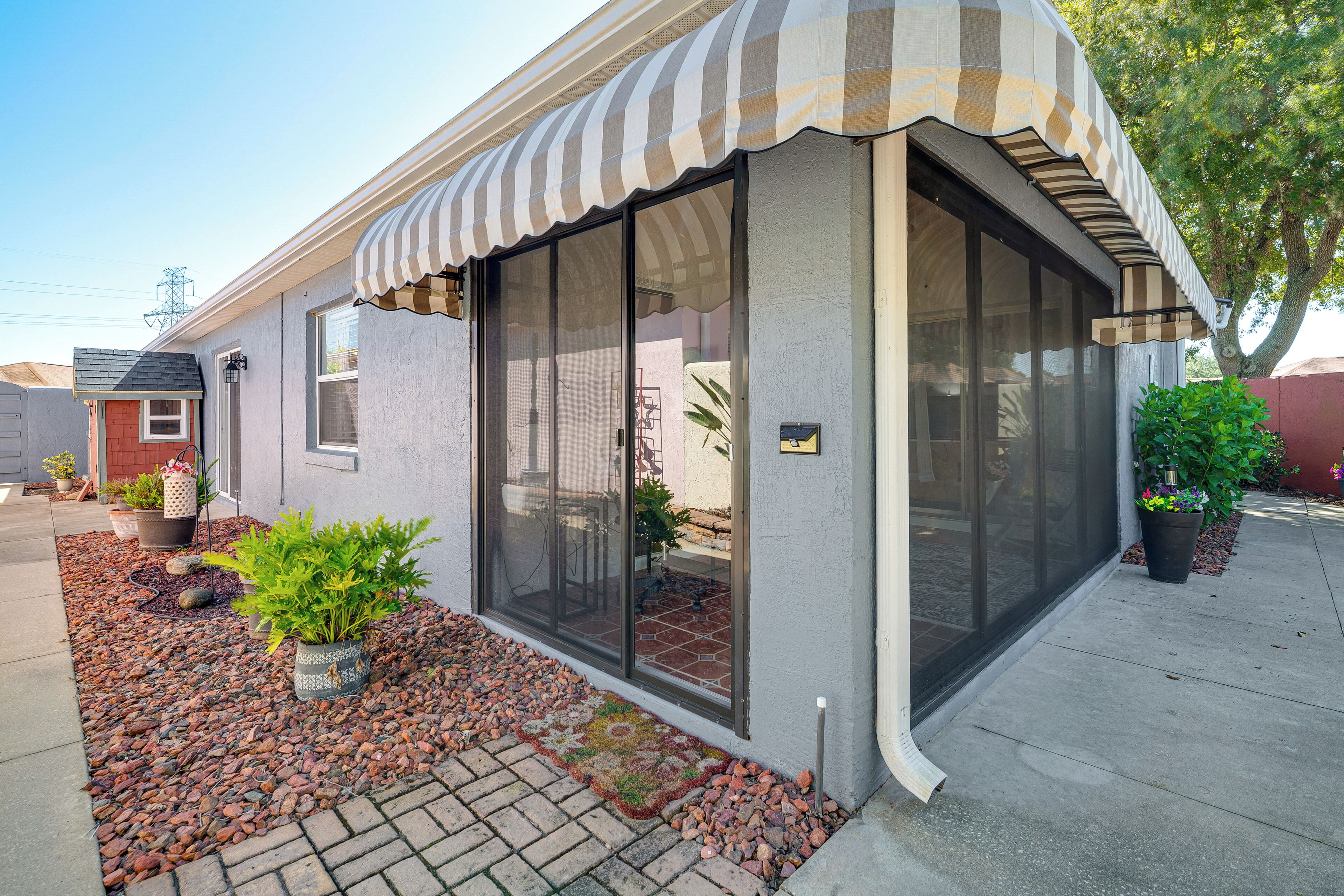 A house with a covered patio, a small garden with potted plants, and a paved walkway.