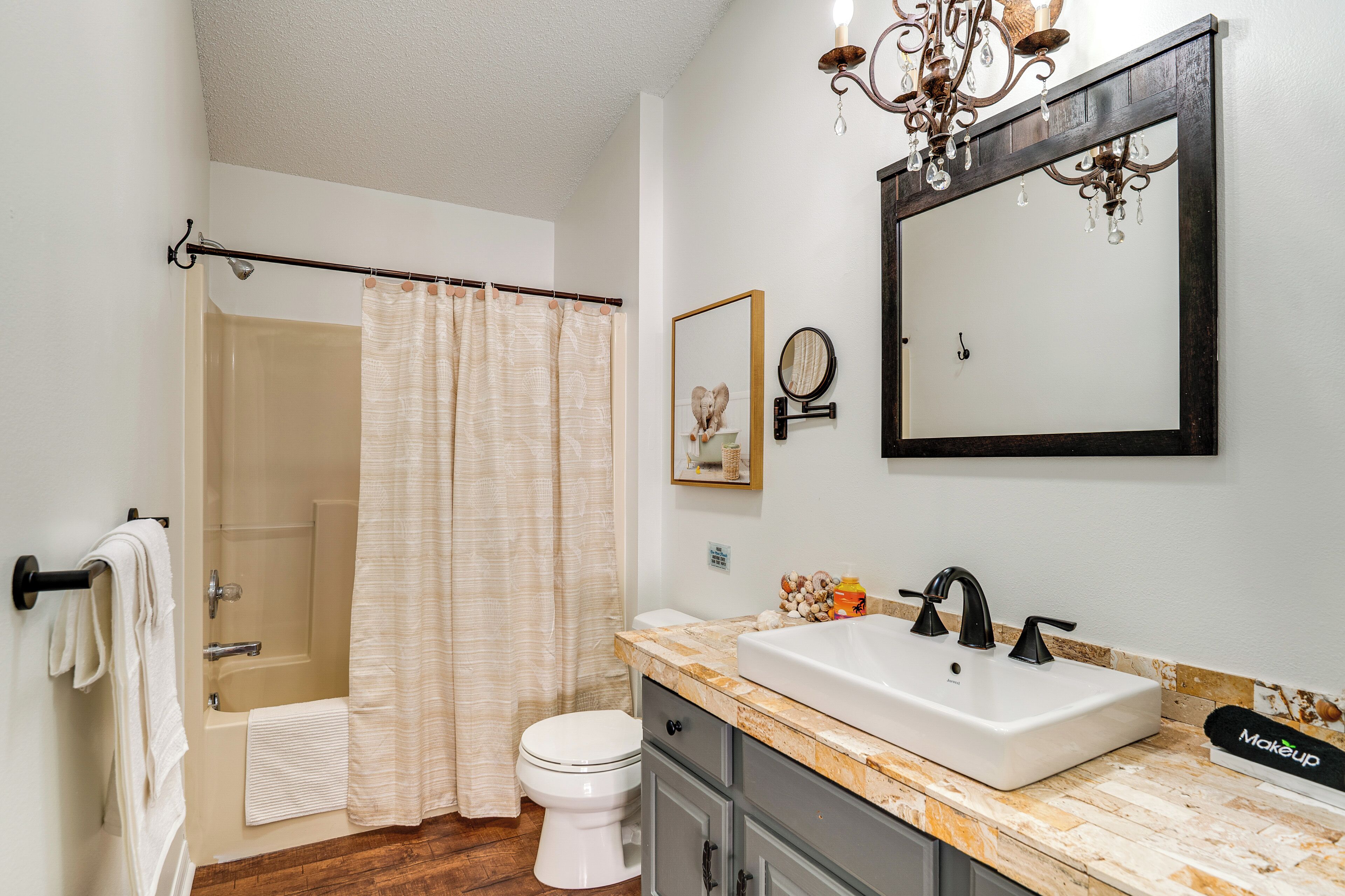 A bathroom with a shower, toilet, sink, and a chandelier.