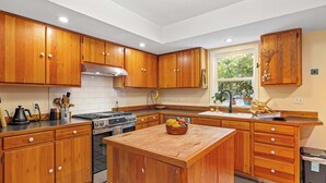 Une cuisine avec des meubles en bois, un îlot central, une cuisinière et une fenêtre donnant sur un paysage verdoyant.