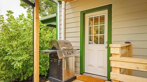 Un espace extérieur abrité, équipé d’un barbecue, d’un banc en bois et d’une porte dont le cadre est vert.