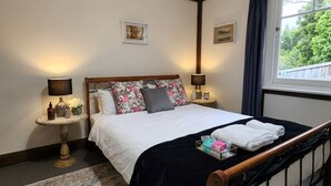 A bedroom with a bed, two bedside tables, a window with curtains, and a view of greenery outside. - Bowen Toft Villa- home-from-home (FIFO friendly) (Sandy Bay)