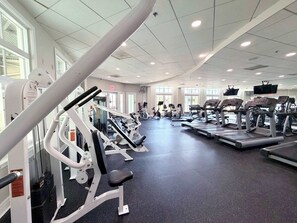 Une salle de sport équipée de divers appareils d’exercice, dotée de grandes fenêtres et d’un plafond pourvu d’un éclairage encastré.