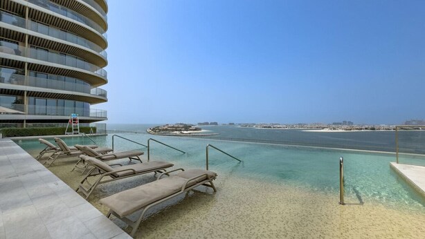 A resort pool with lounge chairs and a view of the sea. - Relaxing Beach Access 1 Bedroom in Grand Bleu (Dubai)