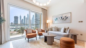 A modern living room with a sofa, armchairs, a coffee table, and a view of a city skyline through large windows. - Relaxing Beach Access 1 Bedroom in Grand Bleu (Dubai)