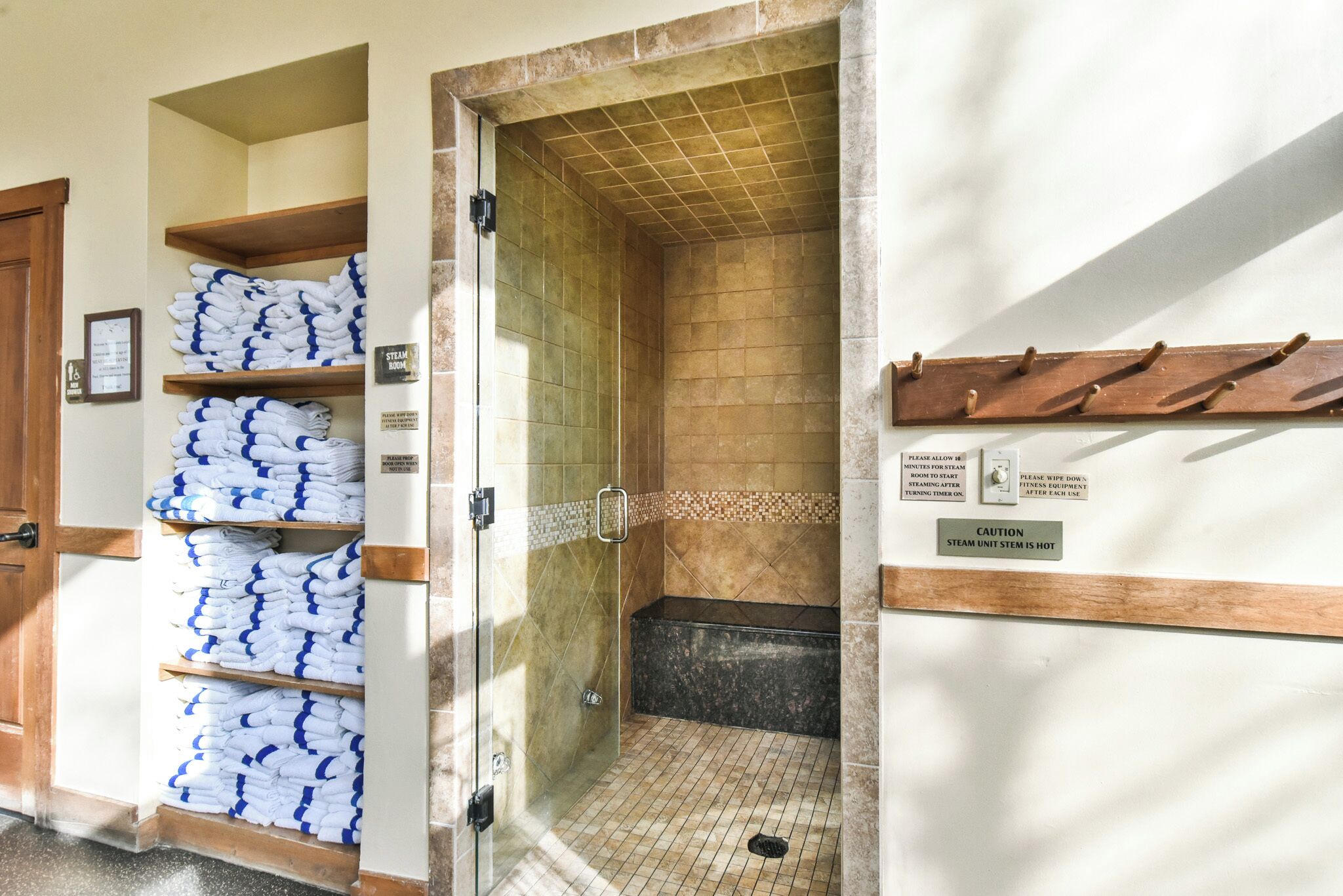 A shower area with a glass door, a tiled wall, and a sign indicating caution about the steam unit's temperature.