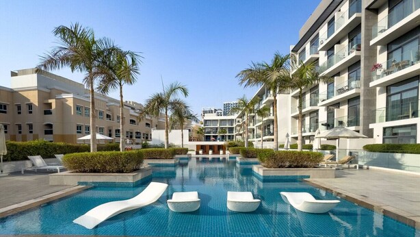 A modern hotel with a central swimming pool, palm trees, and lounge chairs. - Chic Studio in Vibrant Oxford Residence (Dubai)