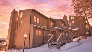 Un edificio de madera de varios pisos con una escalera que lleva a la entrada, rodeado de nieve.