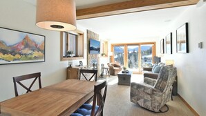 Amplia sala de estar con una mesa de comedor de madera, un sillón estampado y un gran ventanal con vistas a la montaña.