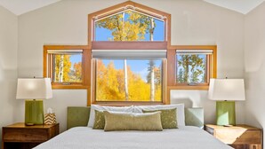 A bedroom with a large bed, two nightstands, a window with a view of autumn trees, and a skylight above. - Back Road Bliss - Beautiful Frisco Home (Frisco)