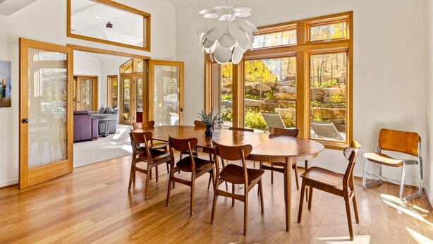 A dining area with a wooden table and chairs, large windows with a view of a garden, and a modern chandelier. - Back Road Bliss - Beautiful Frisco Home (Frisco)