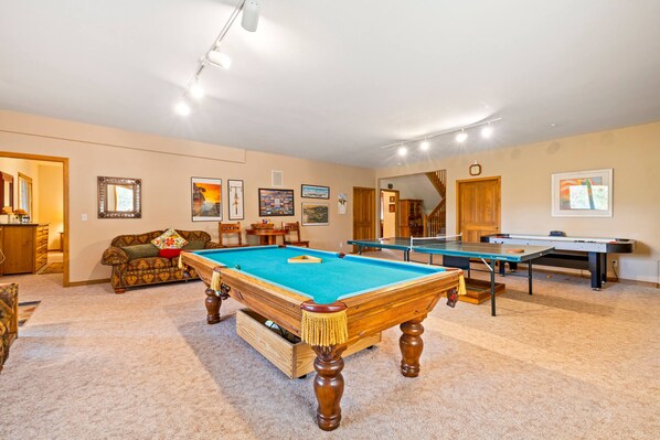 A pool table with a blue felt surface, a wooden sofa with a patterned cushion, and a wooden coffee table.
