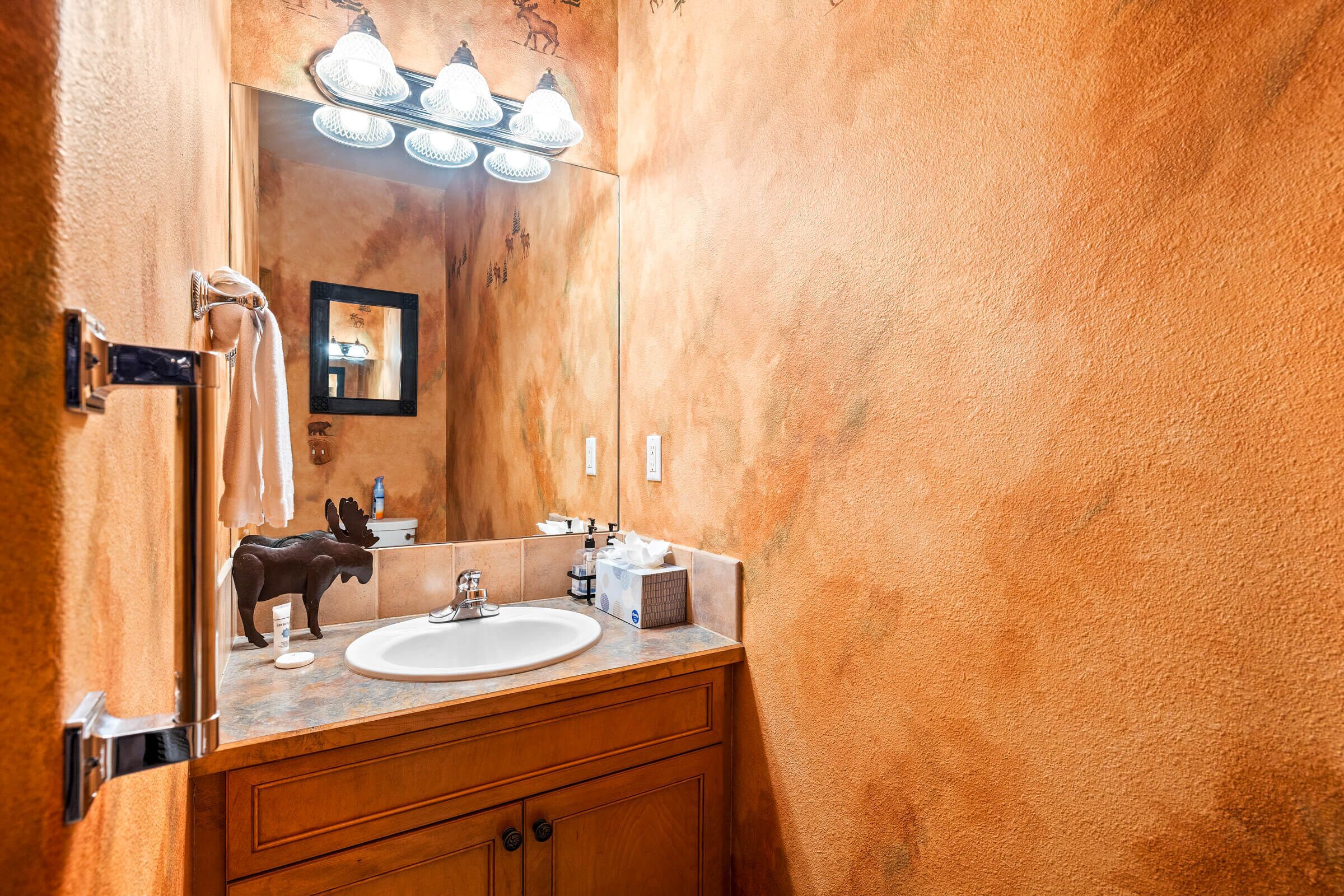 A bathroom with a wooden vanity, a white sink, and a mirror with lights above.