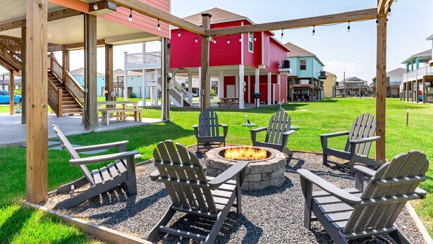 Un espace extérieur abrité, doté de fauteuils Adirondack, d’un foyer et d’une pergola en bois.