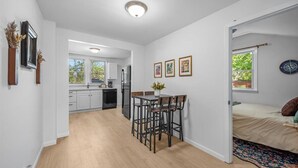 A modern kitchen with white cabinets, a dining area with a table and chairs, and a bed with a view.