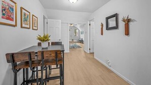 A modern interior with a dining area featuring a wooden table and chairs, white walls, and a hallway leading to other rooms.