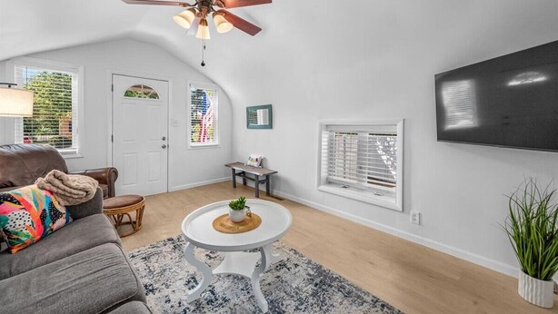 A living room with a ceiling fan, a TV mounted on the wall, a sofa, a coffee table, and a window with blinds.