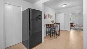 A modern kitchen with a black refrigerator, wooden flooring, and a dining area with a table and chairs.