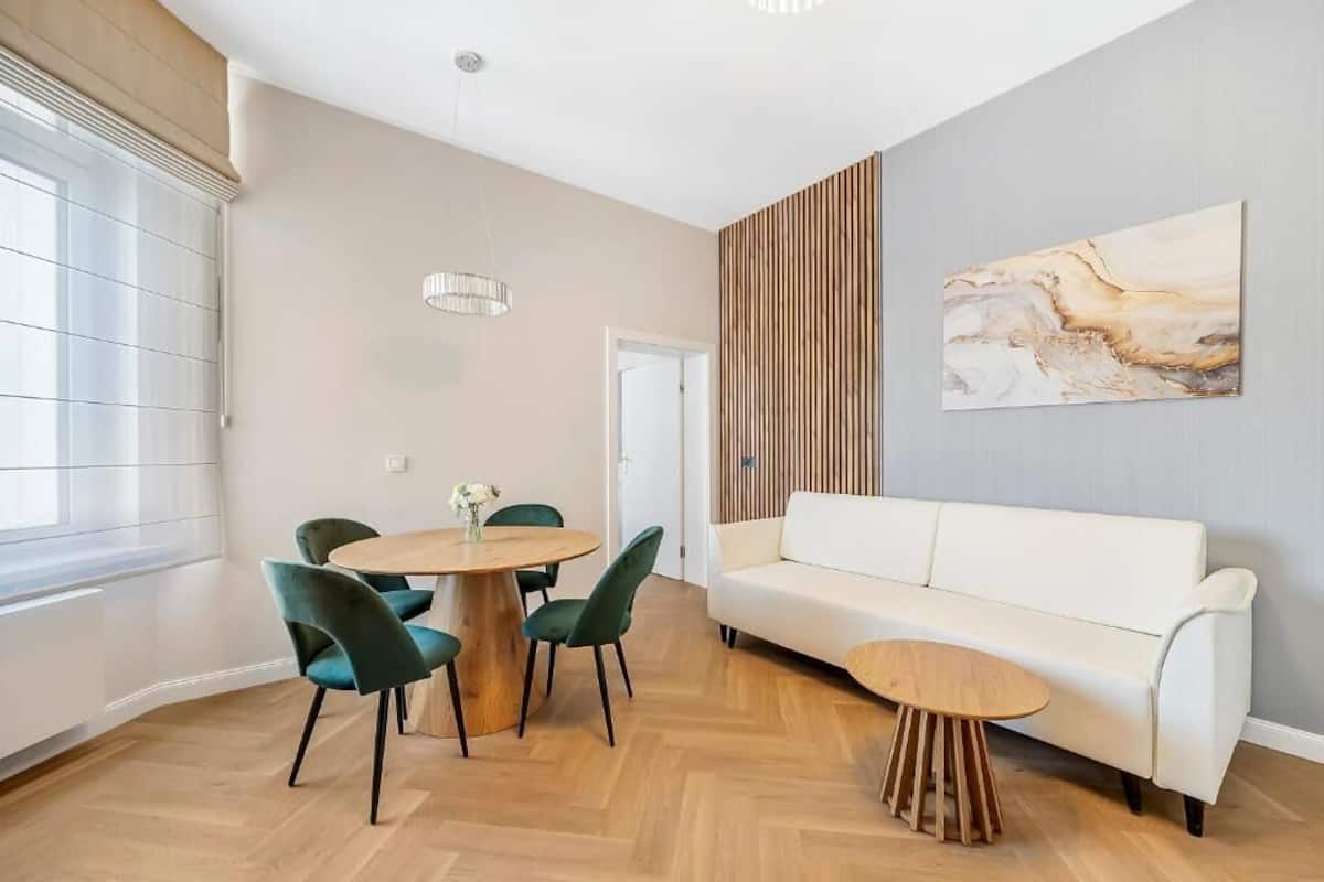 Una sala de estar moderna con un sofá blanco, una mesa de comedor redonda de madera y un cuadro abstracto grande en la pared.