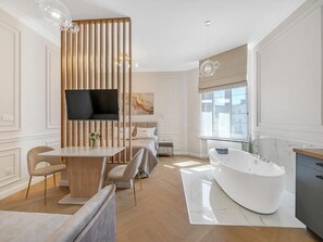 Egy modern fürőszoba, melyben egy különálló, lábas fürdőkád, egy mosdó és egy nagy ablak található, mely természetes fényt biztosít.