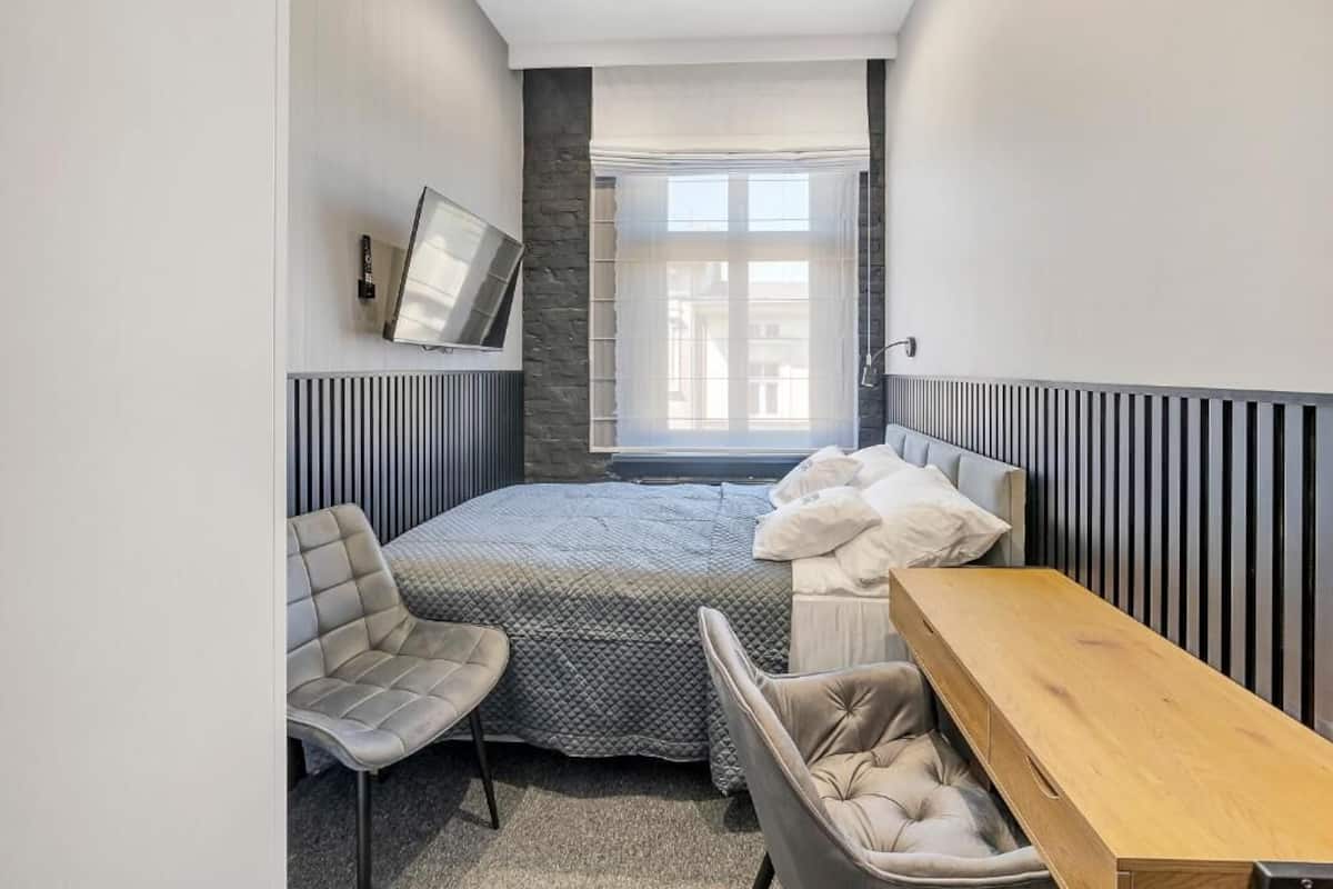 Un dormitorio pequeño con una cama, una mesita de noche, una silla y un televisor montado en la pared.