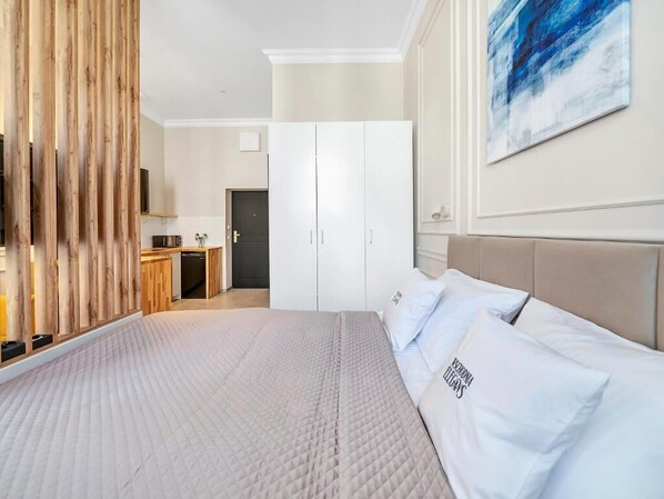 A bedroom with a large bed, a wardrobe, a desk, and a painting on the wall. - Wschodnia Elegans Aparthotel (Łódź)